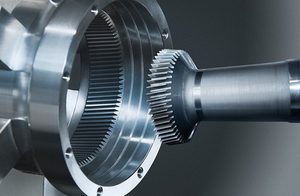 Nahaufnahme einer metallischen Verzahnung, bei der eine Welle mit Stirnrad in ein innenverzahntes Bauteil eingesetzt ist.