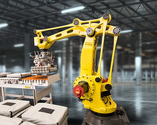 Ein gelber FANUC‑Industrieroboter mit Greifersystem steht in einer Industriehalle und hebt mehrere Säcke von einer Förder- oder Ablagestation an. Neben dem Roboter sind gestapelte Säcke, eine Zuführeinheit und die Hallenstruktur im Hintergrund sichtbar.